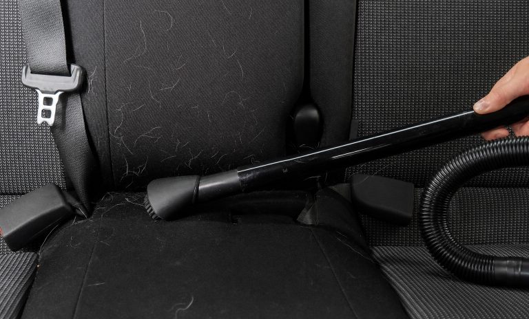 Removing light-colored pet hair from a black cloth car seat with a vacuum brush tool, car interior detailing and cleaning.