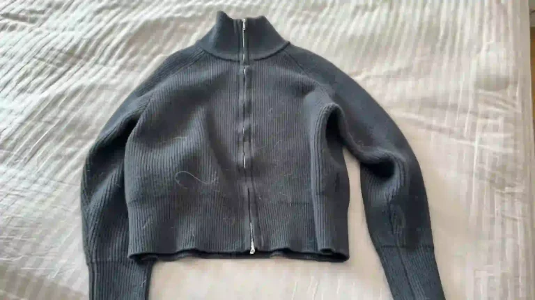 Black zip up knit cardigan covered with pet hair on bed sheet